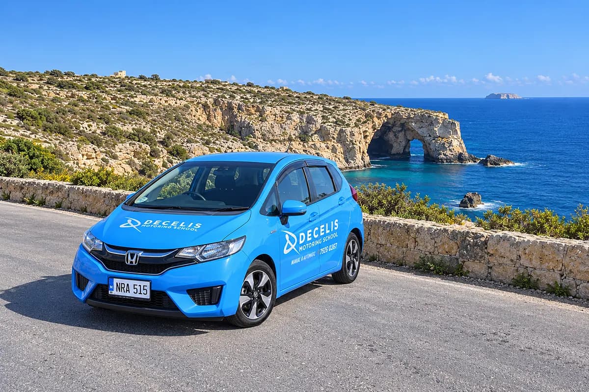 Our blue Honda Jazz, NRA 515, on the coast road above the Blue Grotto, with the rock arch and Filfla on the sea